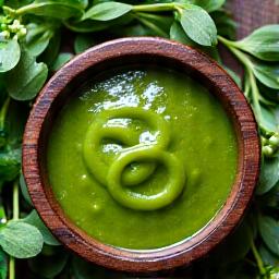 Friske urter og tidlige grønnsaker i vårsolen, som rammer inn en bolle med nylaget ramsløkpesto.